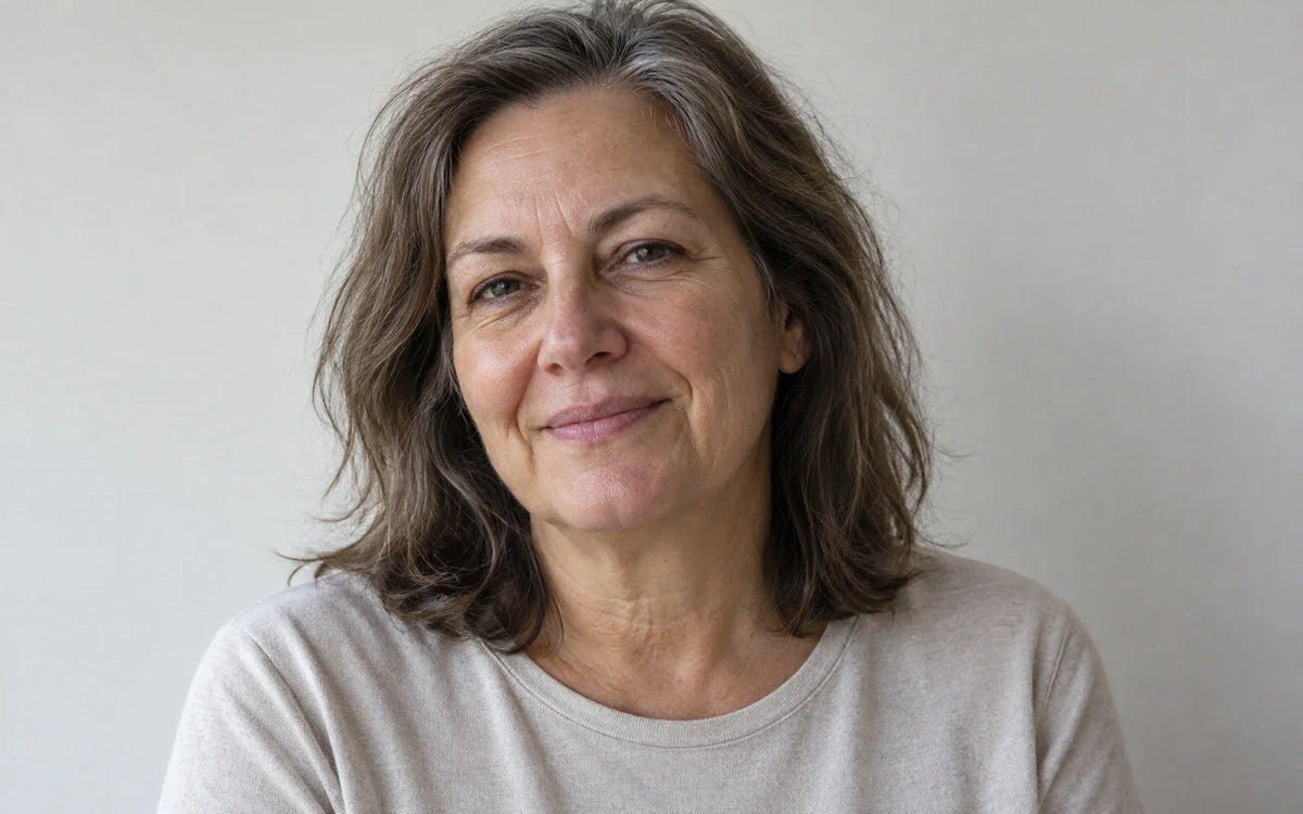 Mujer adulta sonriendo suavemente, con pliegues visibles entre la nariz y las comisuras.